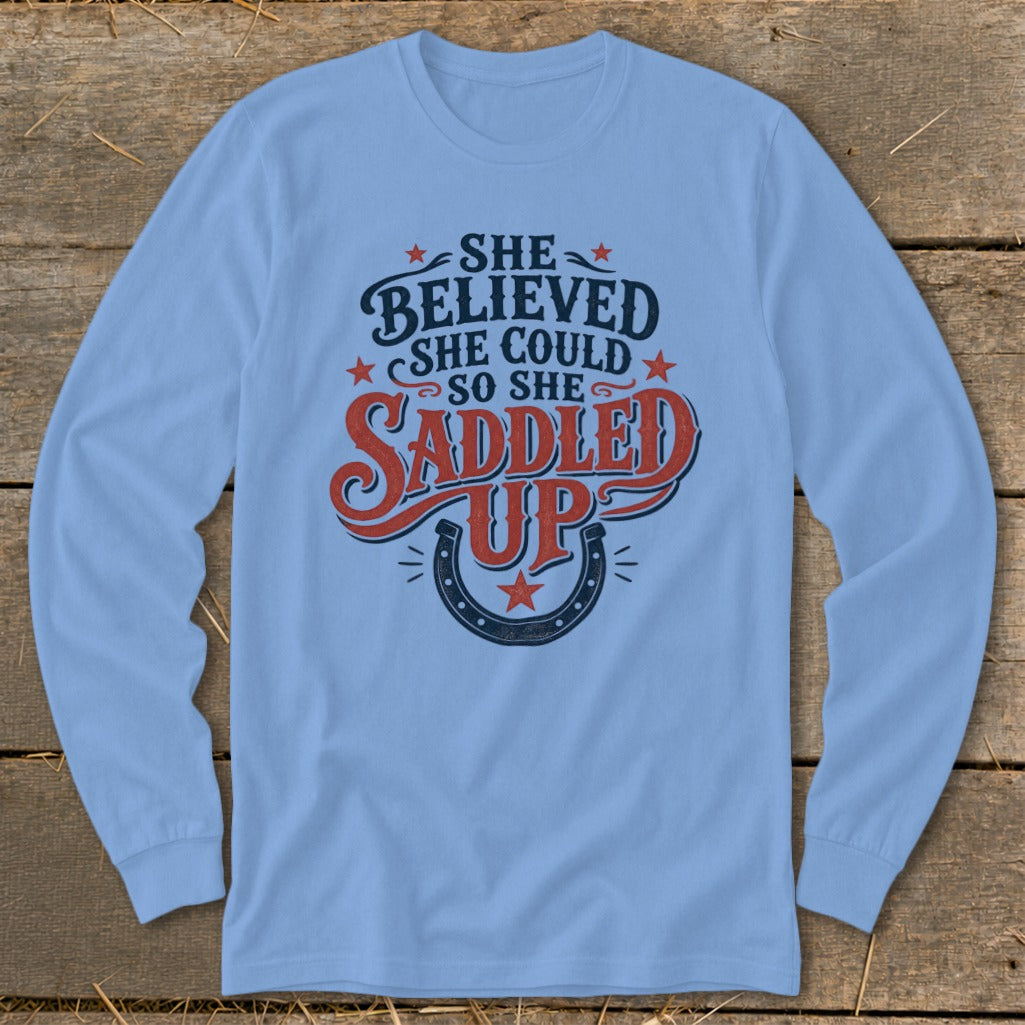 Light blue long-sleeve shirt with "She believed she could so she saddled up" text and horseshoe graphic.