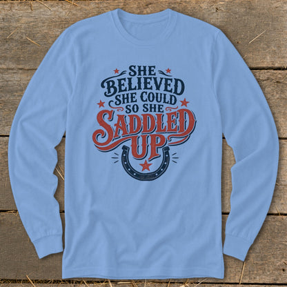 Light blue long-sleeve shirt with "She believed she could so she saddled up" text and horseshoe graphic.
