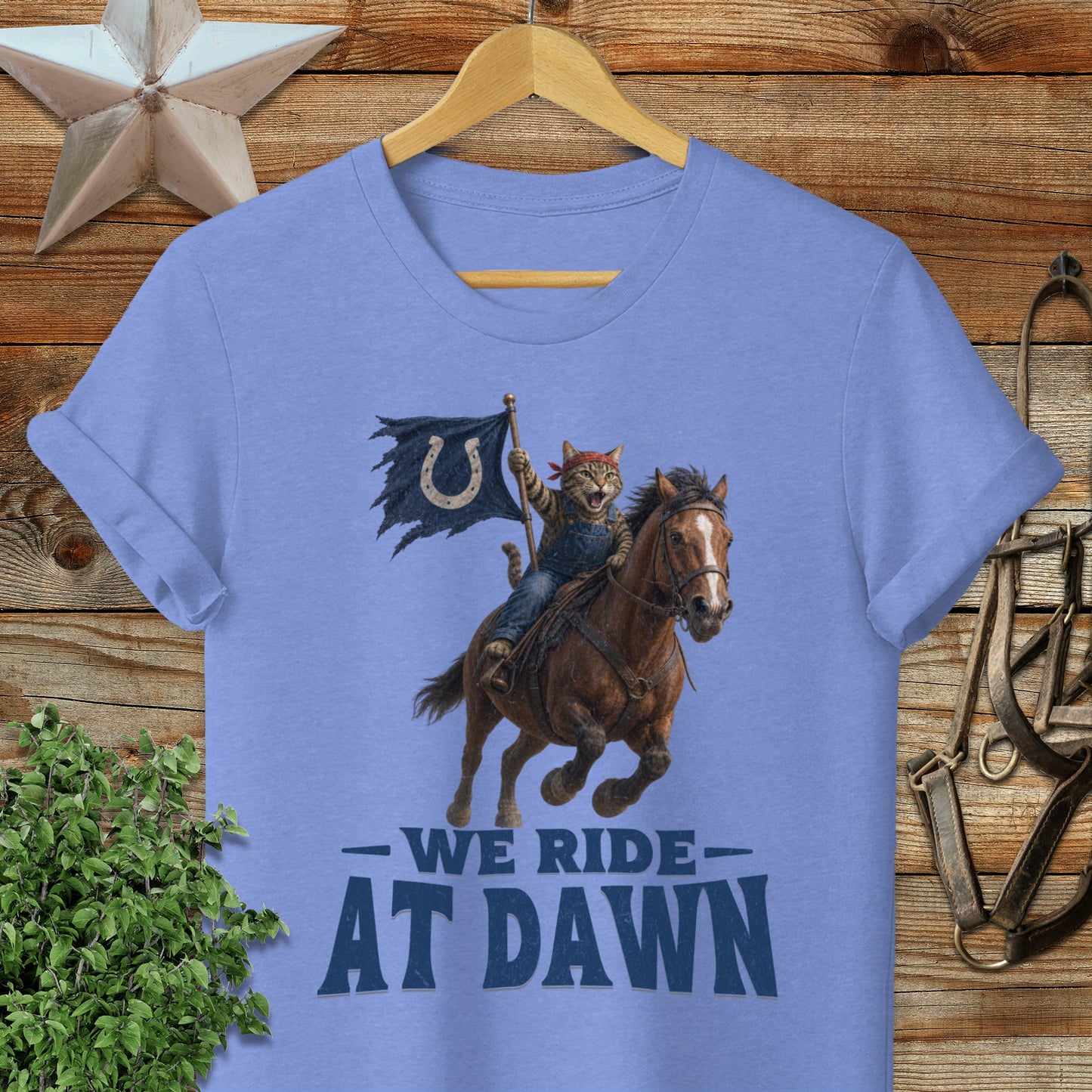 Cat cowboy rides horse, waving flag with horseshoe logo, text "WE RIDE AT DAWN".