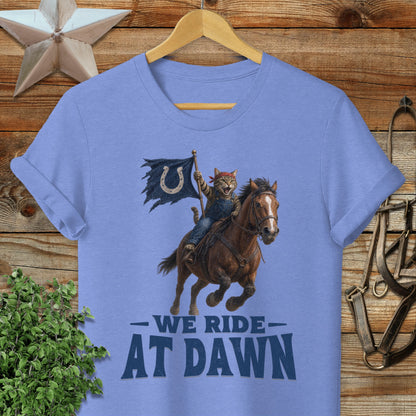 Cat cowboy rides horse, waving flag with horseshoe logo, text "WE RIDE AT DAWN".