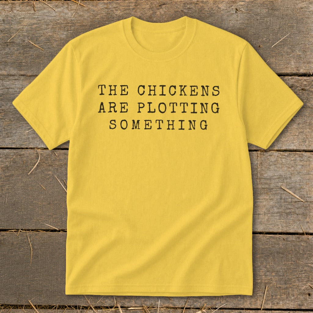 Yellow t-shirt with black text that reads "The Chickens Are Plotting Something."
