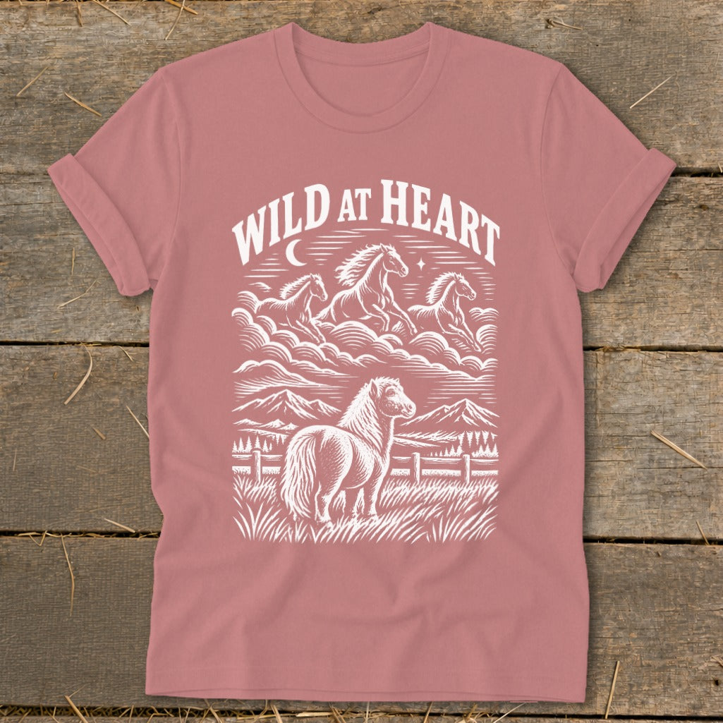 Pink t-shirt with white "Wild at Heart" text and horses in a mountainous landscape.