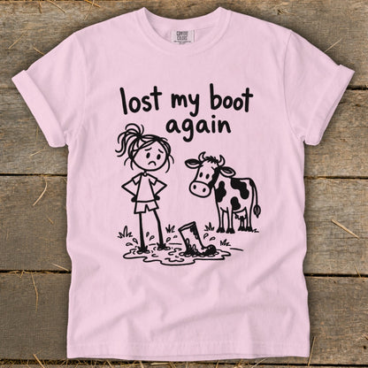 Light pink t-shirt featuring a cartoon of a sad girl standing next to a cow, with the text "lost my boot again".