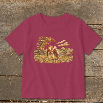 Brown and white horse grazing in an autumn field with colorful leaves and trees.