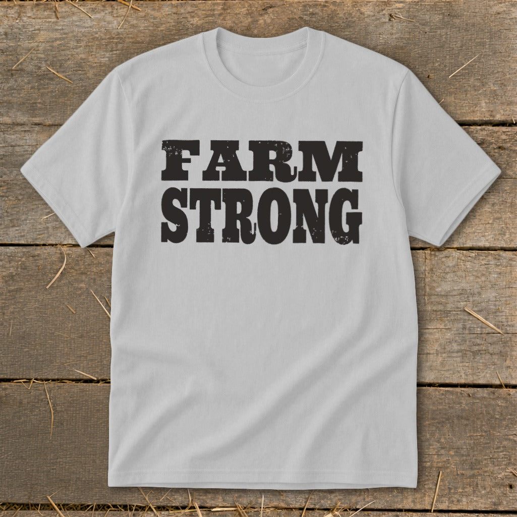 Light gray t-shirt featuring the black distressed text FARM STRONG laid flat on a wooden background.