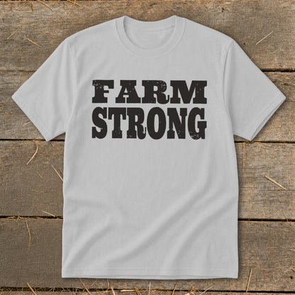 Light gray t-shirt featuring the black distressed text FARM STRONG laid flat on a wooden background.