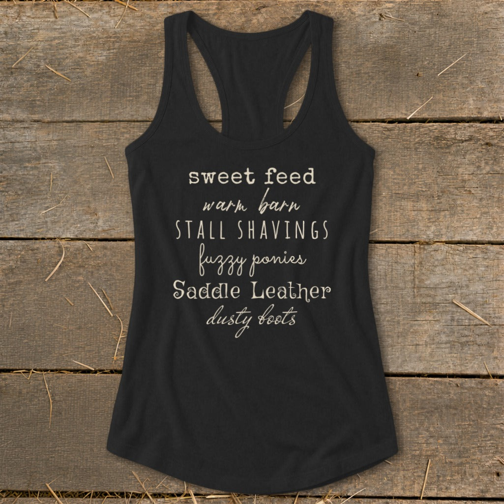 Black tank top with text: "sweet feed warm barn STALL SHAVINGS fuzzy ponies Saddle Leather dusty boots".