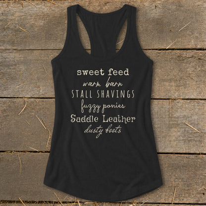Black tank top with text: "sweet feed warm barn STALL SHAVINGS fuzzy ponies Saddle Leather dusty boots".
