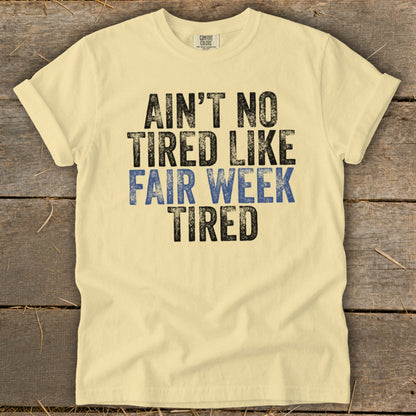 Yellow t-shirt with black and blue text that reads "Ain't no tired like fair week tired".