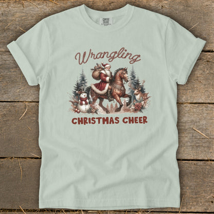 Light green t-shirt with Santa on horseback, snowman, reindeer, and text "Wrangling Christmas Cheer."