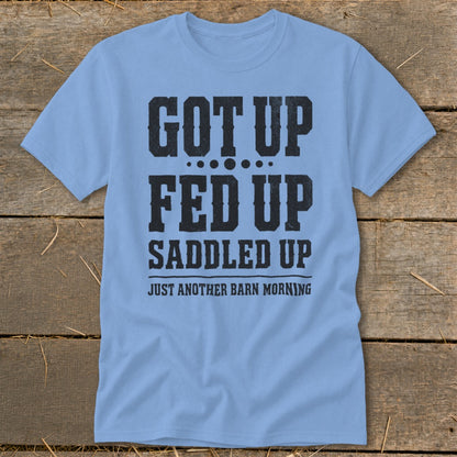 Light blue t-shirt with black text that reads "GOT UP FED UP SADDLED UP JUST ANOTHER BARN MORNING".
