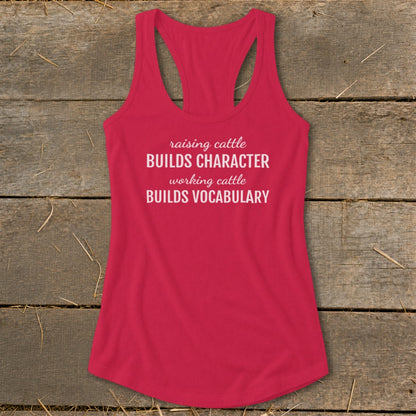 Red racerback tank top with white text reading "raising cattle BUILDS CHARACTER working cattle BUILDS VOCABULARY."