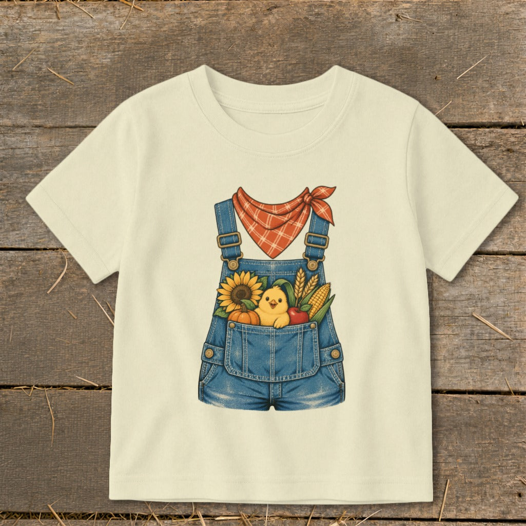 Cream t-shirt with illustration of a chick in denim overalls filled with fall harvest.