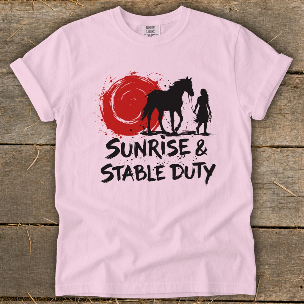 Pink t-shirt with black graphic of horse, rider, and red sun, text "Sunrise & Stable Duty".