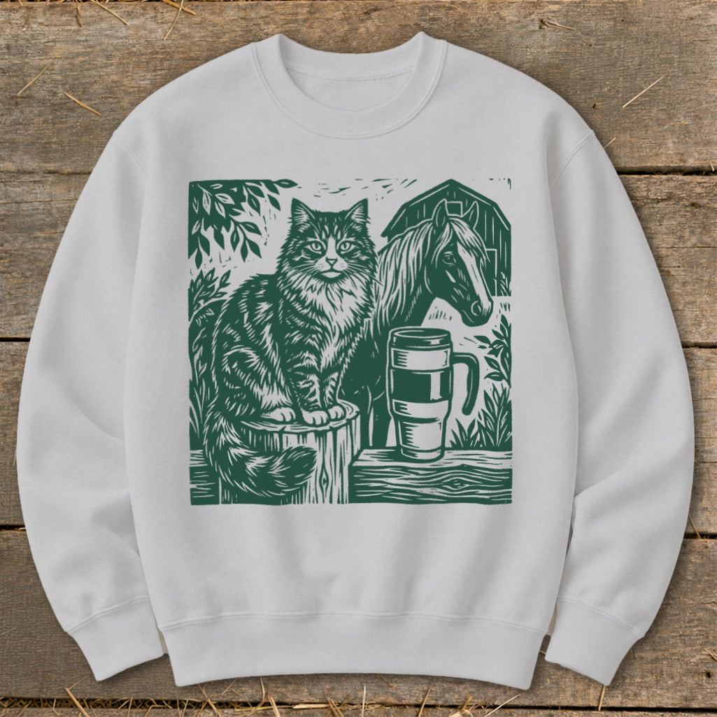 White sweatshirt with green linocut art of a cat, horse, mug, and barn.