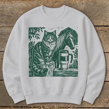 White sweatshirt with green linocut art of a cat, horse, mug, and barn.