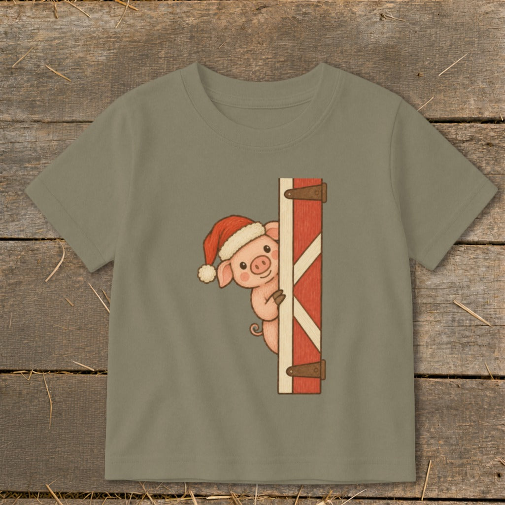 Pig wearing Santa hat peeking from behind a rustic barn door.