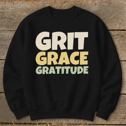 Black crewneck sweatshirt featuring stacked pastel text that reads GRIT GRACE GRATITUDE.