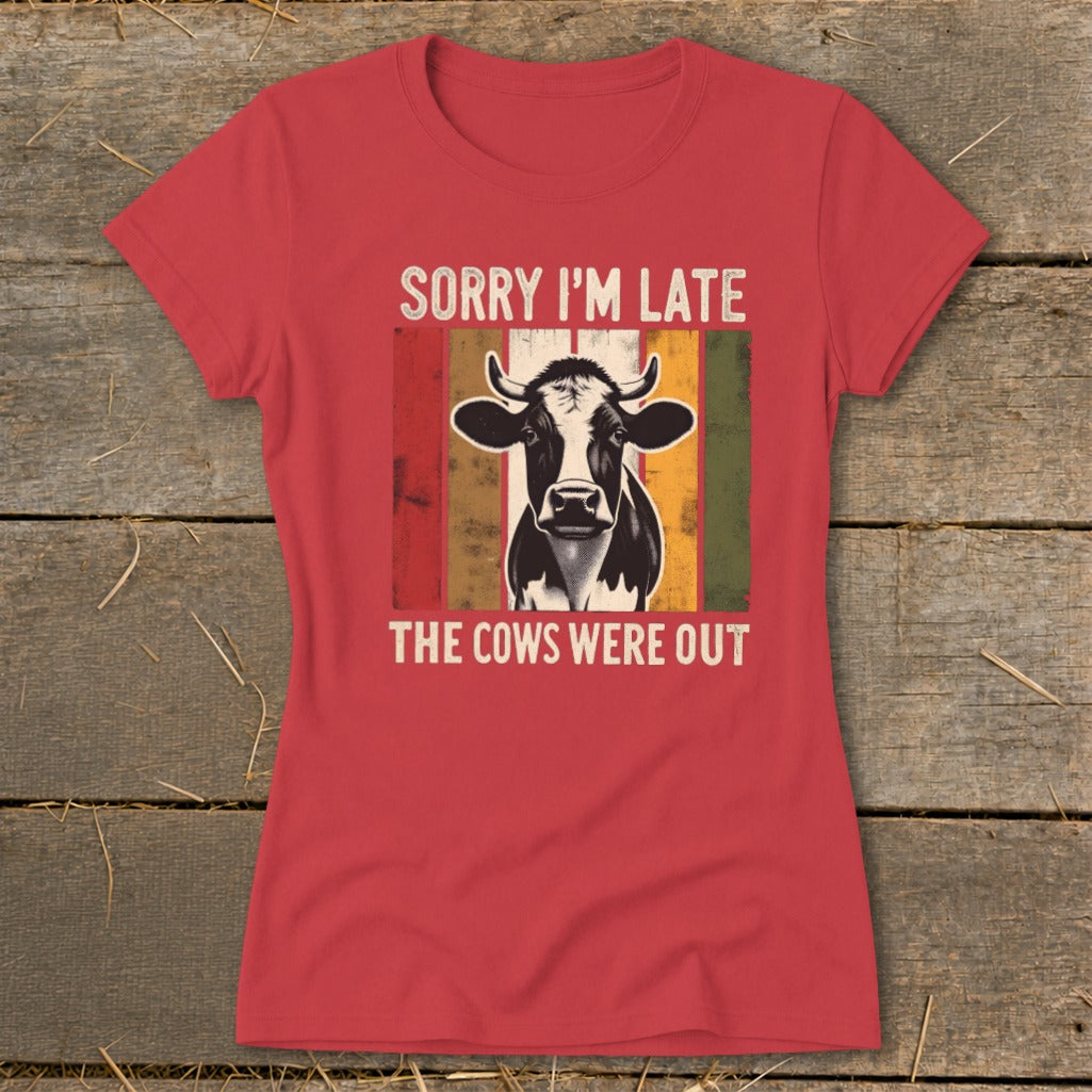 A red t-shirt with a vintage-style graphic of a cow and text that reads SORRY I'M LATE THE COWS WERE OUT.