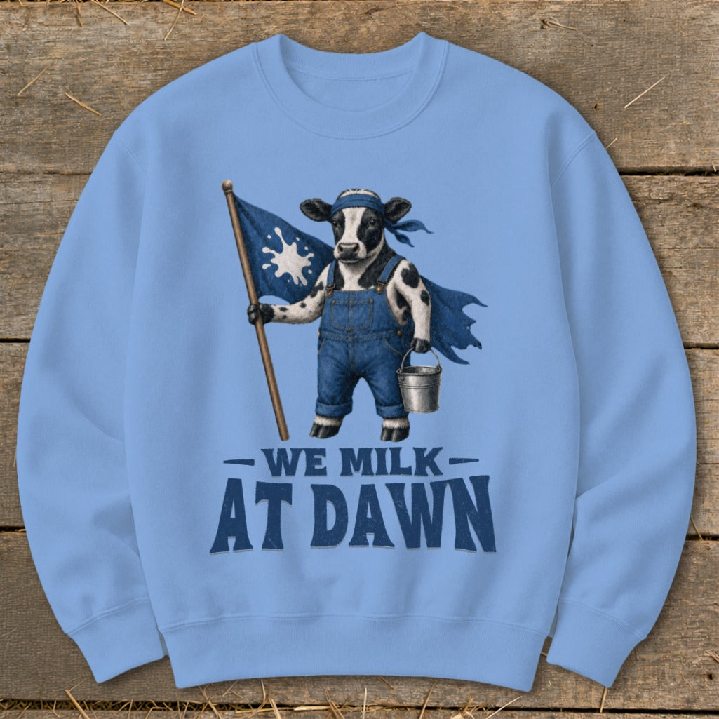 Light blue sweatshirt with a cow holding a milk splash flag and wearing overalls, text reads "WE MILK AT DAWN".