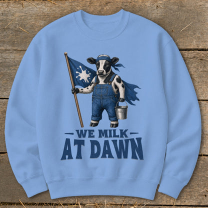 Light blue sweatshirt with a cow holding a milk splash flag and wearing overalls, text reads "WE MILK AT DAWN".