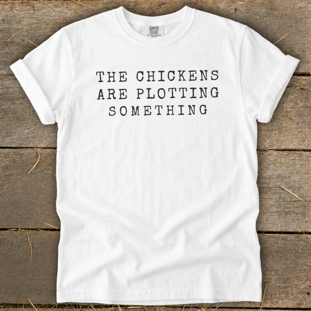 White t-shirt with black text "THE CHICKENS ARE PLOTTING SOMETHING".