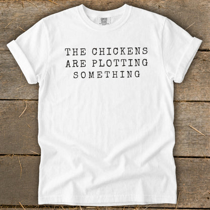 White t-shirt with black text "THE CHICKENS ARE PLOTTING SOMETHING".