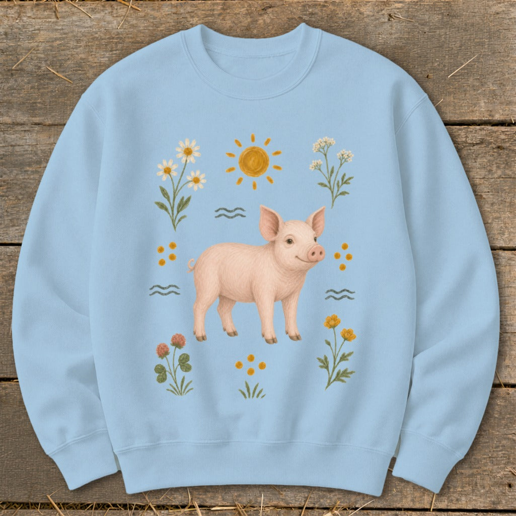Light blue sweatshirt with a pink pig, sun, daisies, and clover illustration.