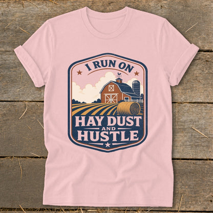 Pink t-shirt with "I RUN ON HAY DUST AND HUSTLE" graphic featuring a barn and hay bale.