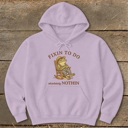 Light purple hoodie with a frog in a rocking chair and text "fixin to do absolutely nothin".