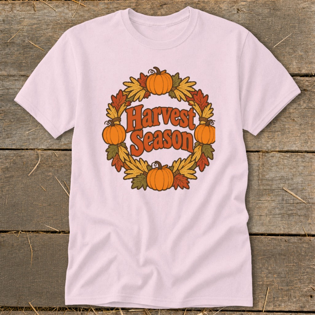 Light pink t-shirt with "Harvest Season" text surrounded by pumpkins and fall leaves wreath.