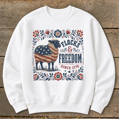 White sweatshirt with a sheep adorned in the American flag, surrounded by floral border. Text reads "Flocks & Freedom Since 1776".