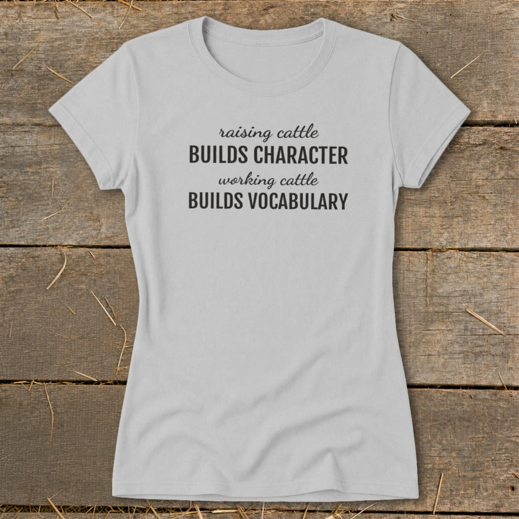 Light gray t-shirt with black text: "raising cattle BUILDS CHARACTER, working cattle BUILDS VOCABULARY."