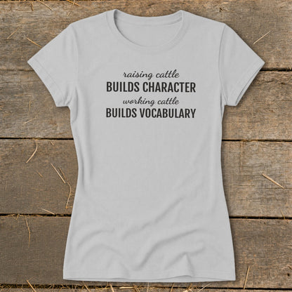 Light gray t-shirt with black text: "raising cattle BUILDS CHARACTER, working cattle BUILDS VOCABULARY."
