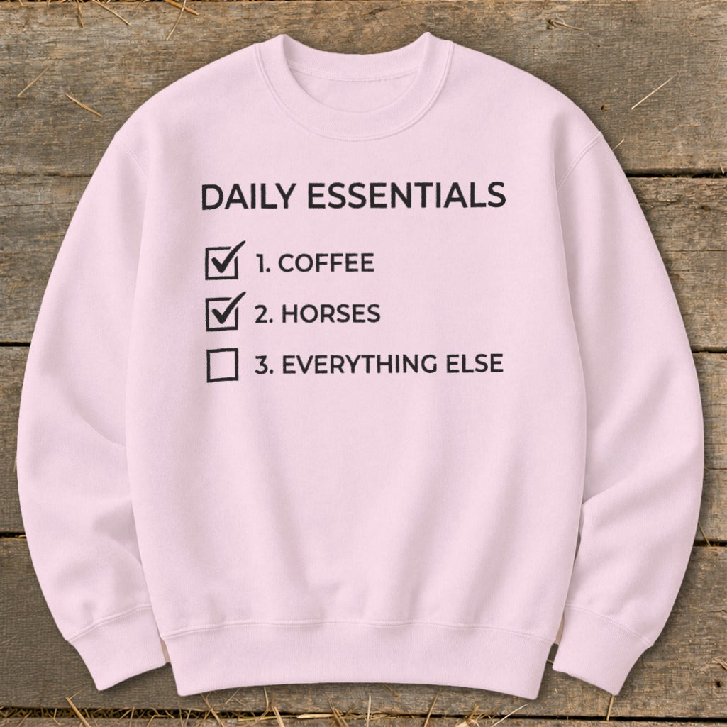 Pink sweatshirt with "Daily Essentials" checklist: coffee and horses checked.