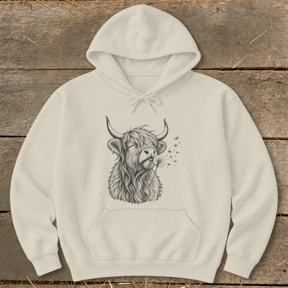 Cream hoodie with sketch of a Highland cow blowing dandelion seeds.
