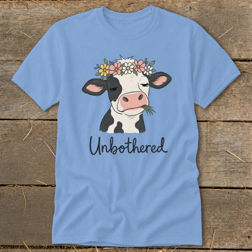 Light blue t-shirt with a cow wearing a flower crown and eating grass, text "Unbothered".
