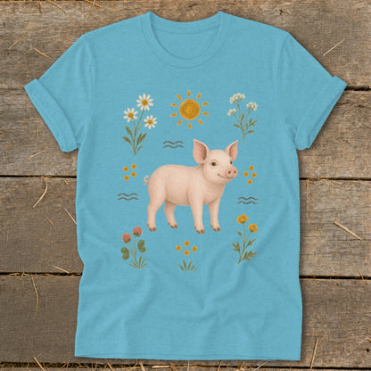 Light blue t-shirt with a piglet surrounded by daisies, clover, and a sun illustration.
