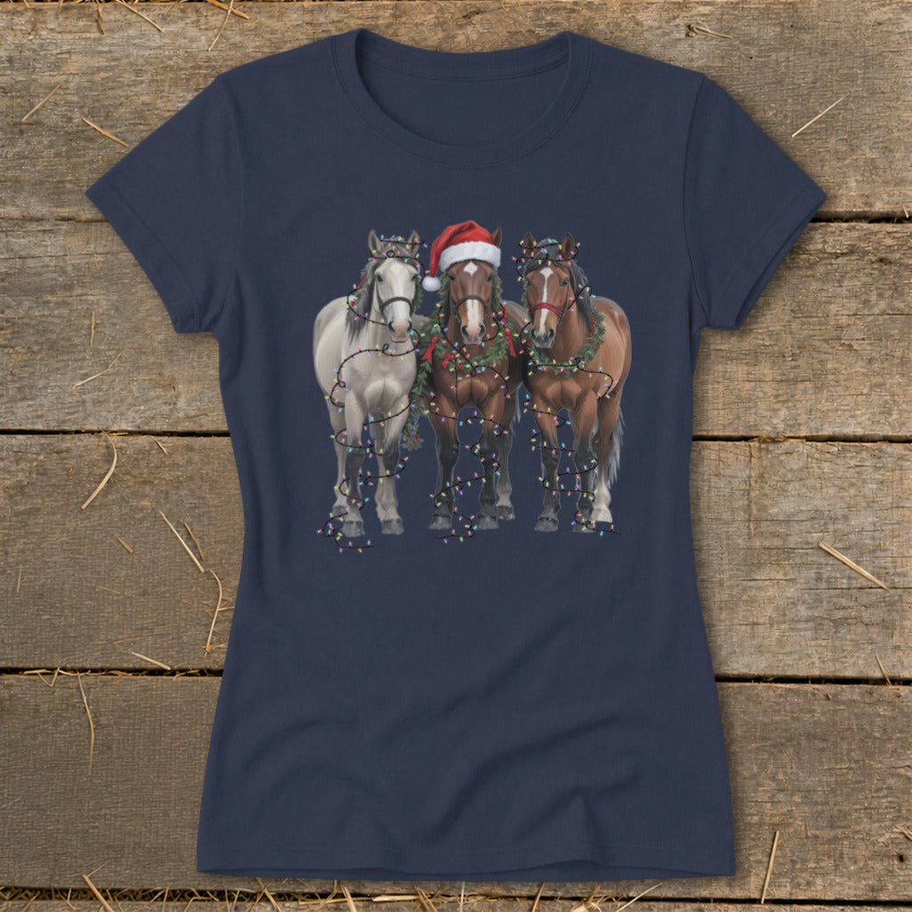 Three horses, one with a Santa hat, decorated with Christmas lights and garland.