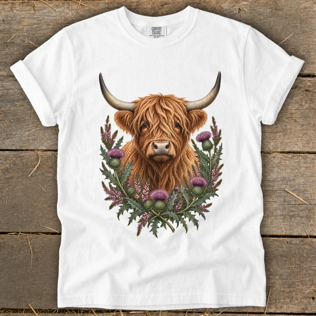 Highland cow illustration surrounded by thistles on a white t-shirt.