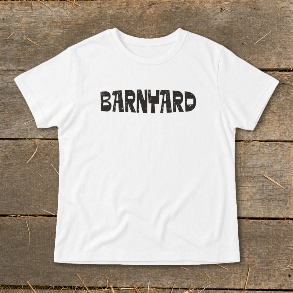 A white short-sleeved t-shirt with the word "BARNYARD" printed in black, distressed block letters across the chest, laid flat on a rustic wooden background.
