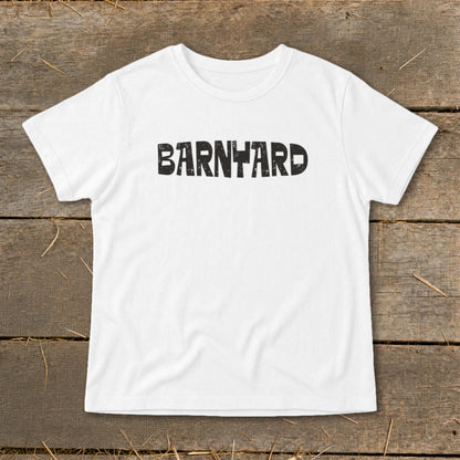 A white short-sleeved t-shirt with the word "BARNYARD" printed in black, distressed block letters across the chest, laid flat on a rustic wooden background.