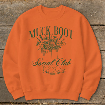 Orange sweatshirt with green "Muck Boot Social Club" text and floral design.