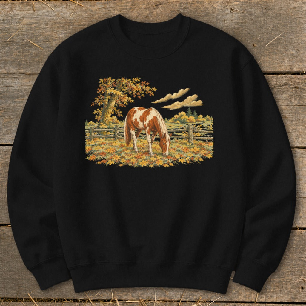 Brown and white horse grazing in a field of fallen autumn leaves near a fence.