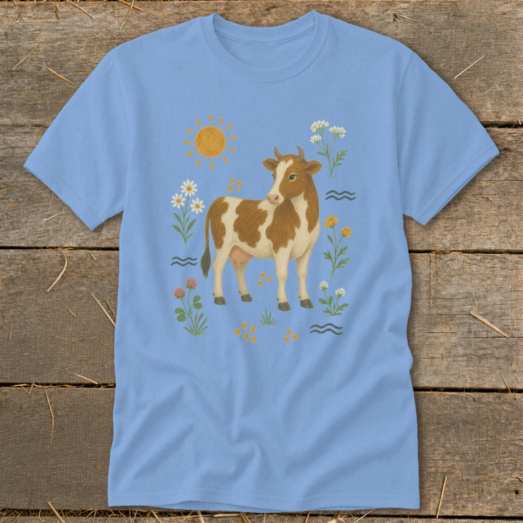 Light blue t-shirt with a brown and white cow surrounded by flowers and sun.