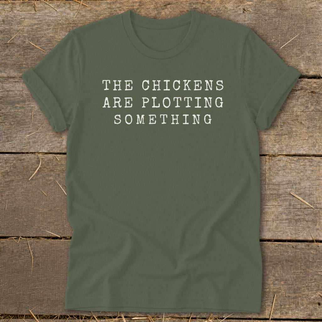 Olive green t-shirt with white text that reads "THE CHICKENS ARE PLOTTING SOMETHING".