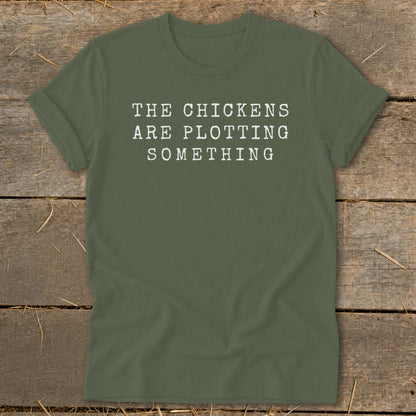 Olive green t-shirt with white text that reads "THE CHICKENS ARE PLOTTING SOMETHING".