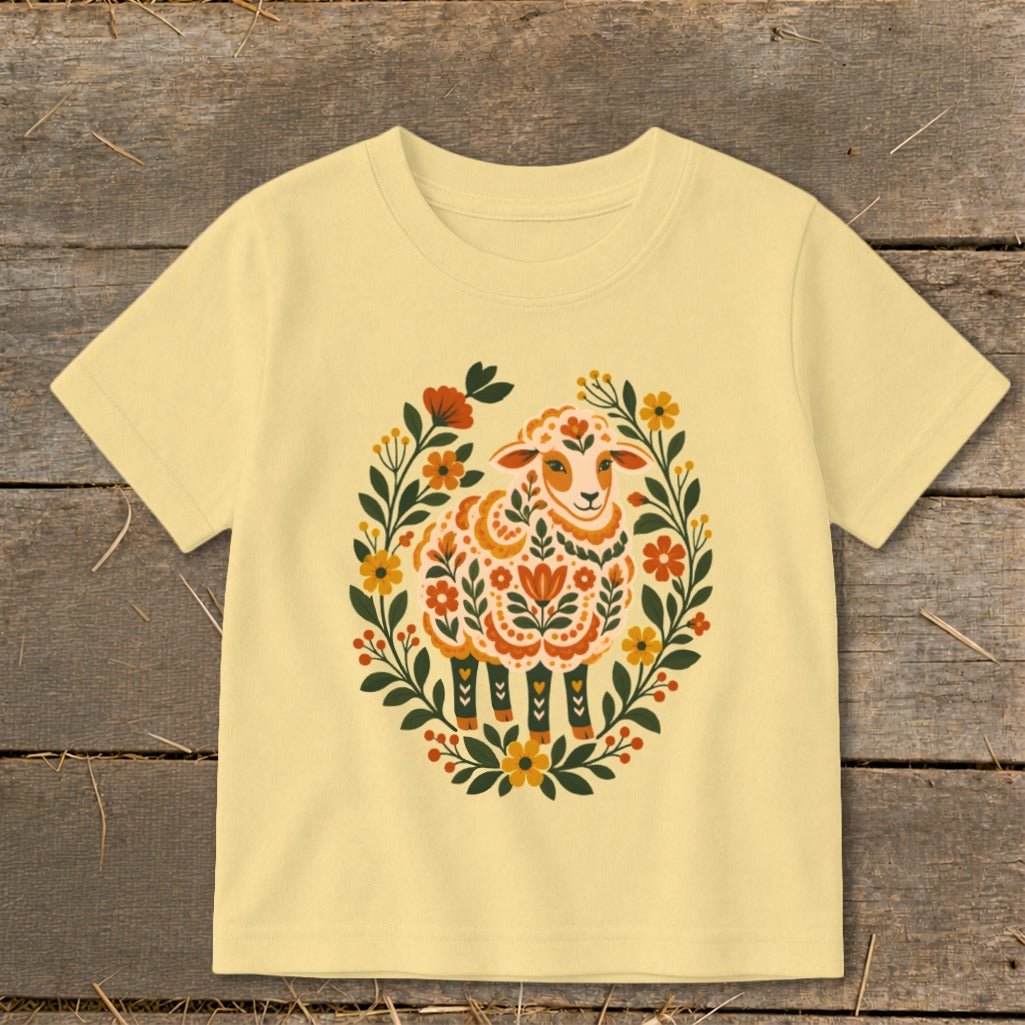 Yellow t-shirt featuring a folk art sheep surrounded by a floral wreath.
