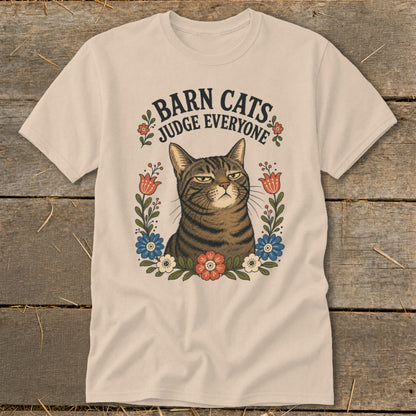 Barn Cats Judge Everyone graphic on a tan t-shirt featuring a grumpy tabby cat surrounded by flowers.