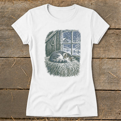 T-shirt graphic of a cat sleeping on hay in front of a snowy window.
